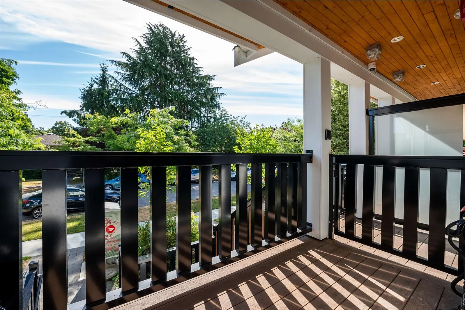 White dome camera on a wood porch soffit, with a black access device on the pillar beside a metal gate.