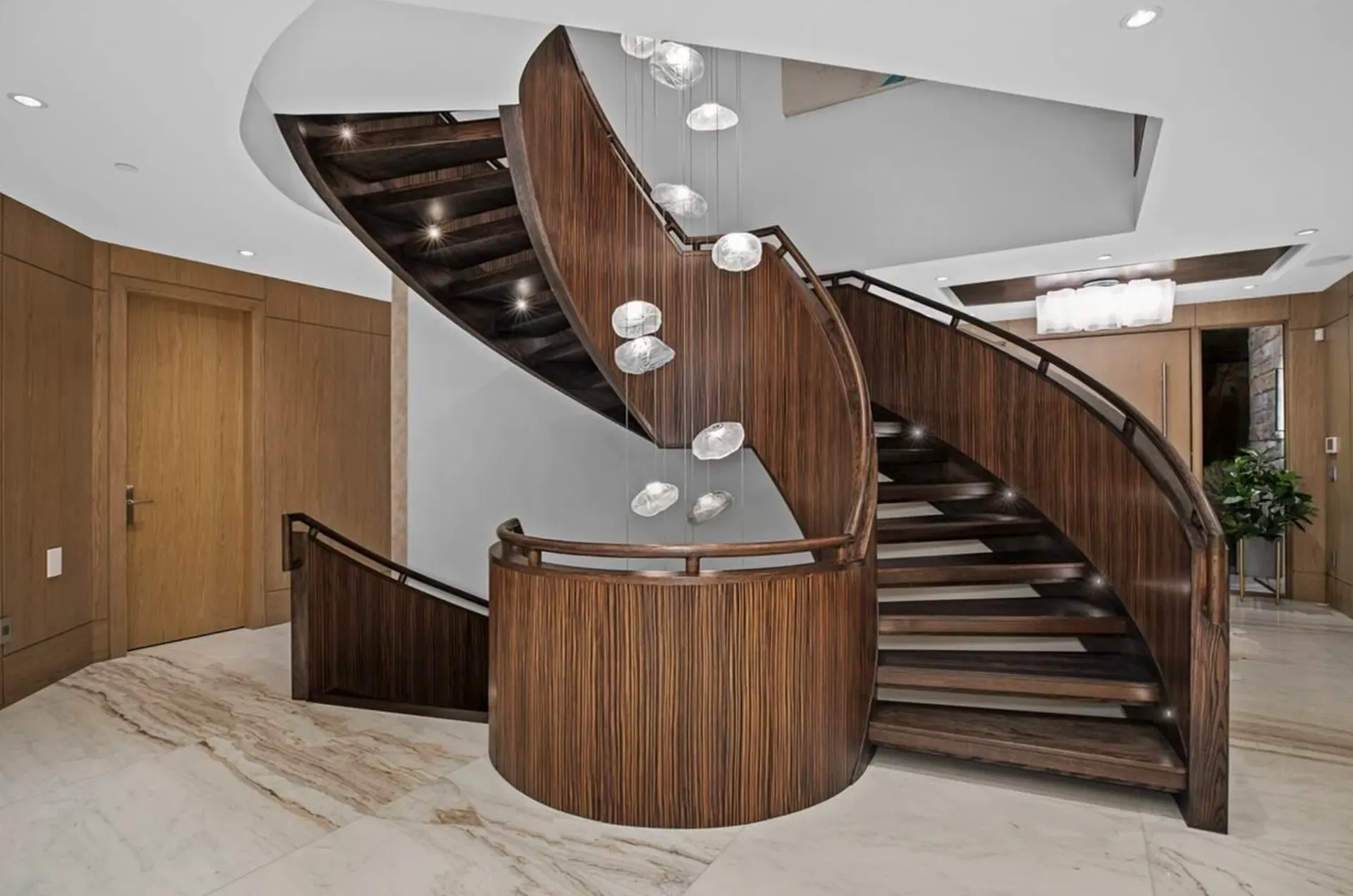 Curved wood staircase with step lights and a cascade of glass pendants.